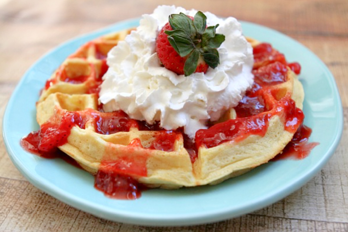 waffle on plate topped with strawberry sauce and whipped cream