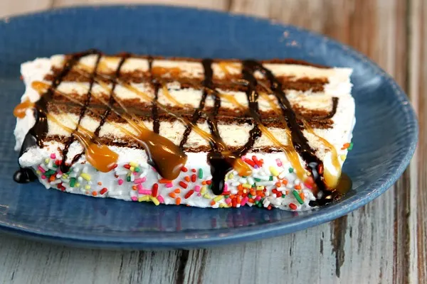 slice of ice cream sandwich cake topped with caramel and hot fudge on a blue plate