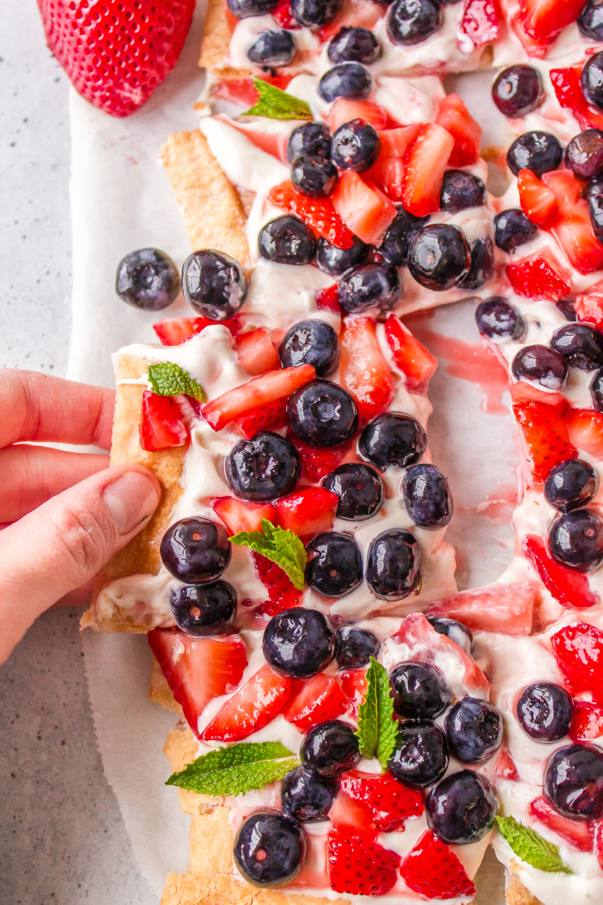 hand pulling out piece of berry cheesecake tart out of whole thing