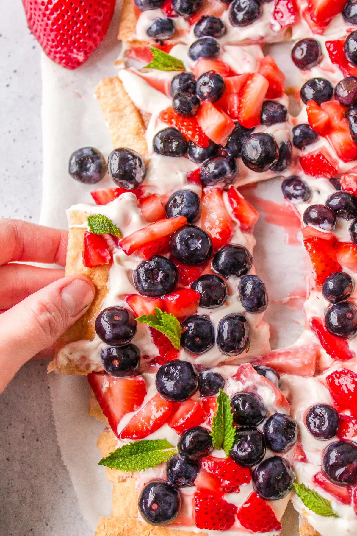 hand pulling out piece of berry cheesecake tart out of whole thing