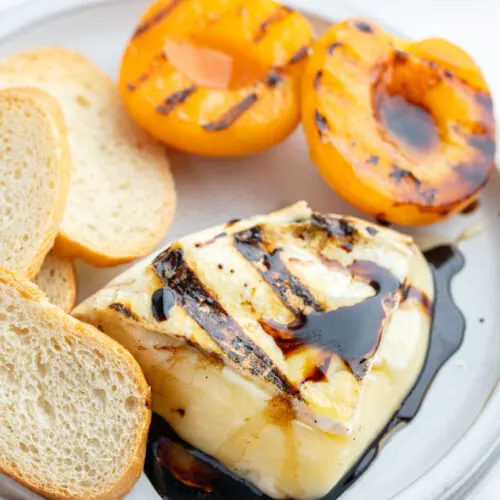 chunk of melted brie on plate with balsamic glaze, baguette and grilled apricots