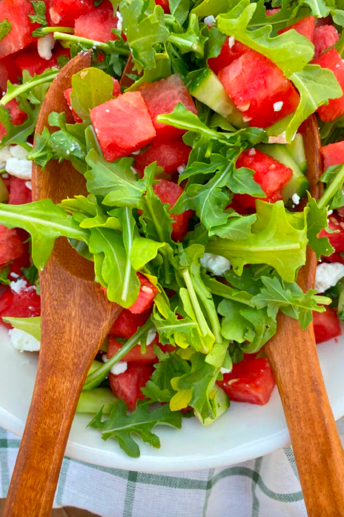 watermelon cucumber and feta arugula salad in bowl with salad tongs