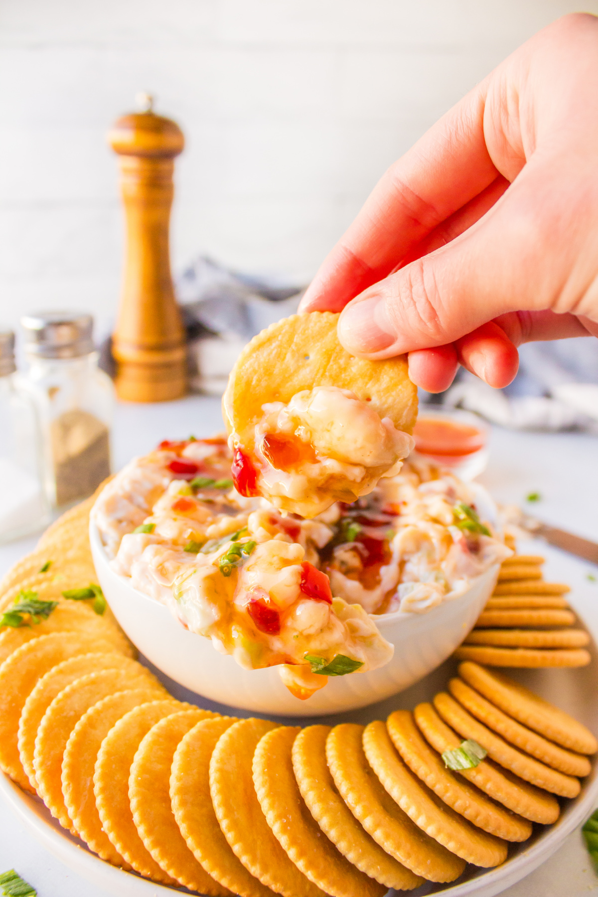 hand dipping cracker into pepper jelly cream cheese dip