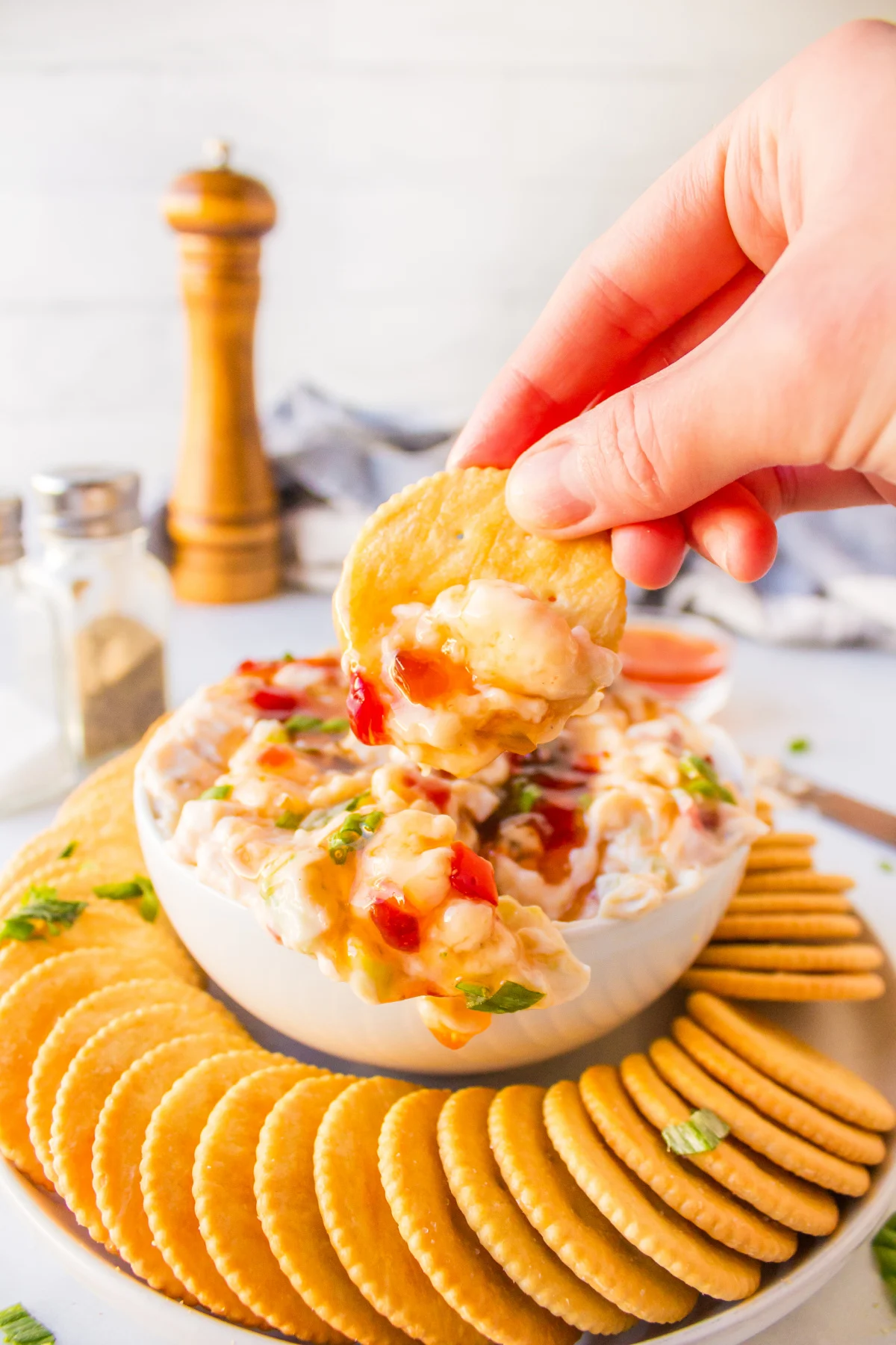 hand dipping cracker into pepper jelly cream cheese dip